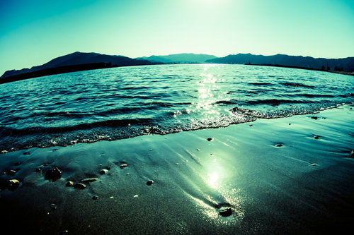 波打ち際に反射する日の光と砂浜、山並みと太陽光のライン
