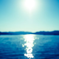 サンセット時に海面に映る太陽光のボケた光と水面の風景の写真