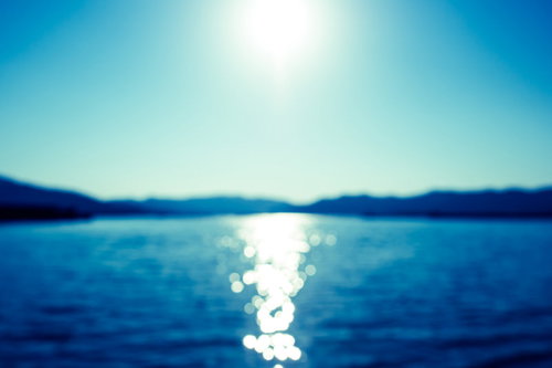 サンセット時に海面に映る太陽光のボケた光と水面の風景の写真