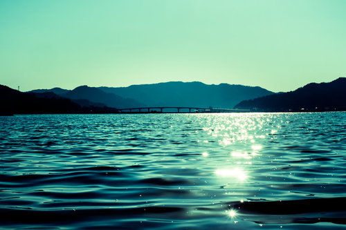 穏やかな宇佐湾に架かる橋と朝日、浜辺から見た海岸風景