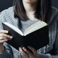 グレーのニットセーターを着て洋書を読む女性の写真
