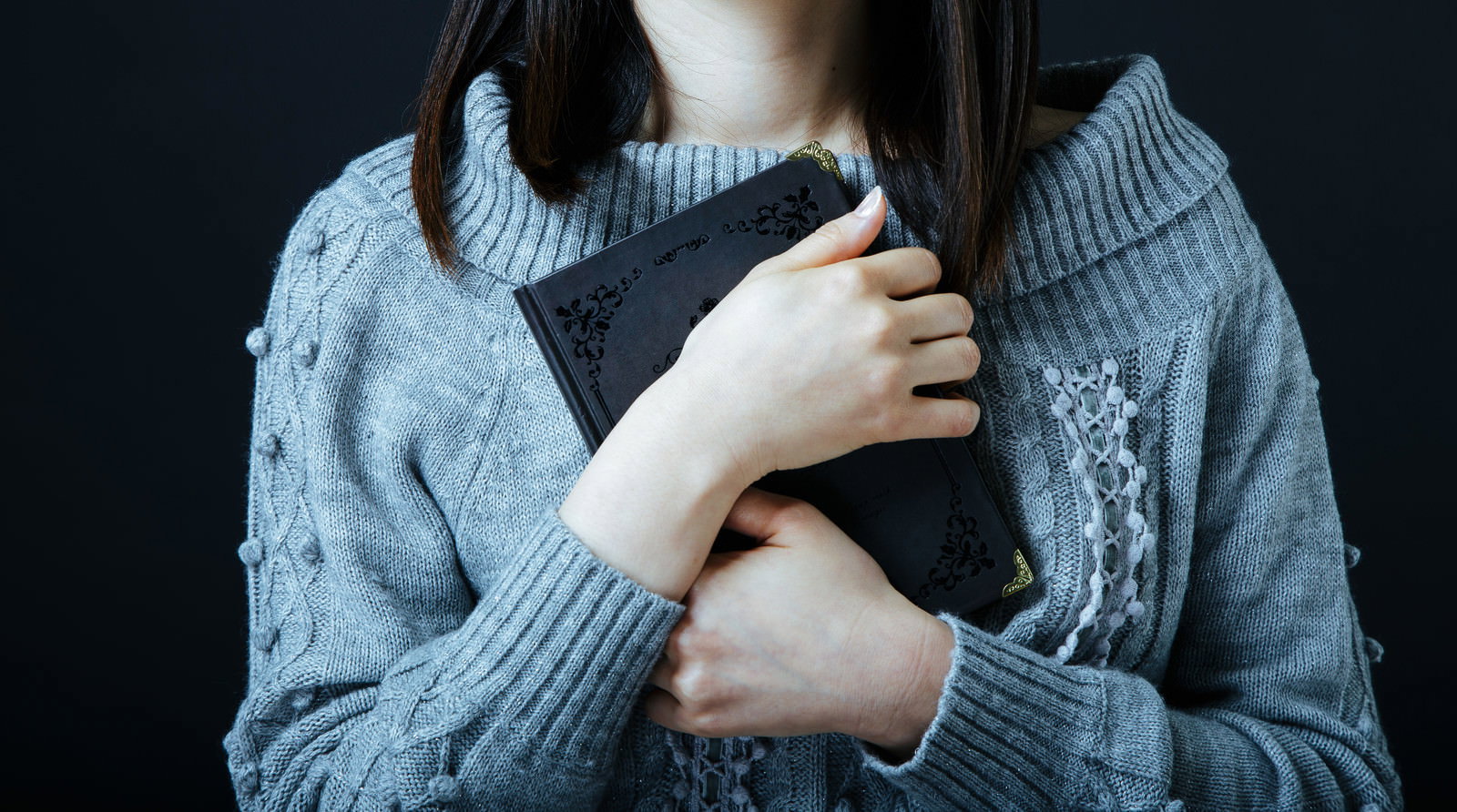 グレーのニットを着た女性が黒いノートを胸元で抱きしめている様子