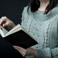 グレーのニットを着て洋書をめくる女性の手元の写真