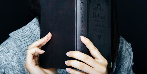 グレーのセーターを着た女性が洋書を手に取る