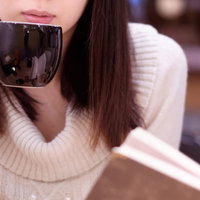 カフェでコーヒーを飲みながら読書する女性の写真
