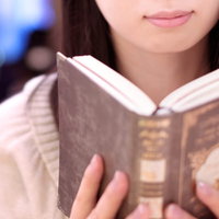 カフェでピンクのパーカーを着て洋書を読む女性の写真