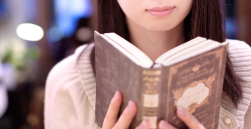カフェでピンクのパーカーを着て洋書を読む女性