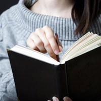 黒い洋書に栞をはさむグレーのニット姿の女性の写真