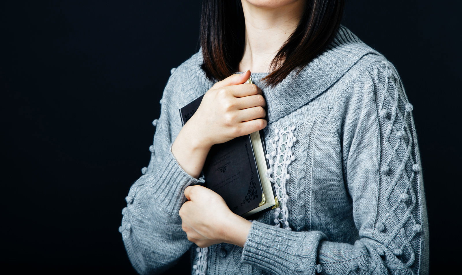 グレーのケーブル編みカーディガンを着て本を持つ女性