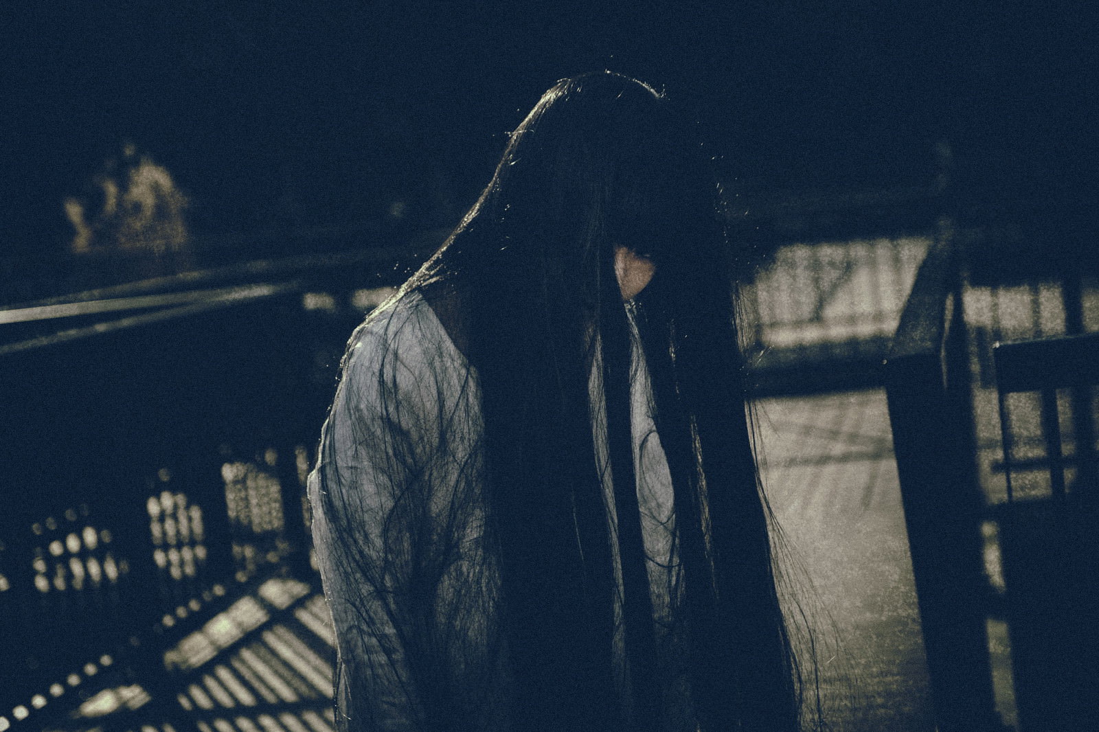 長い黒髪で顔を覆った白装束の女性が暗闇でこちらを見つめている［モデル：緋真煉］