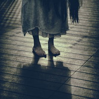 不気味な裸足で立つ女性の足元、薄暗い木製の床に映る呪いの影の写真