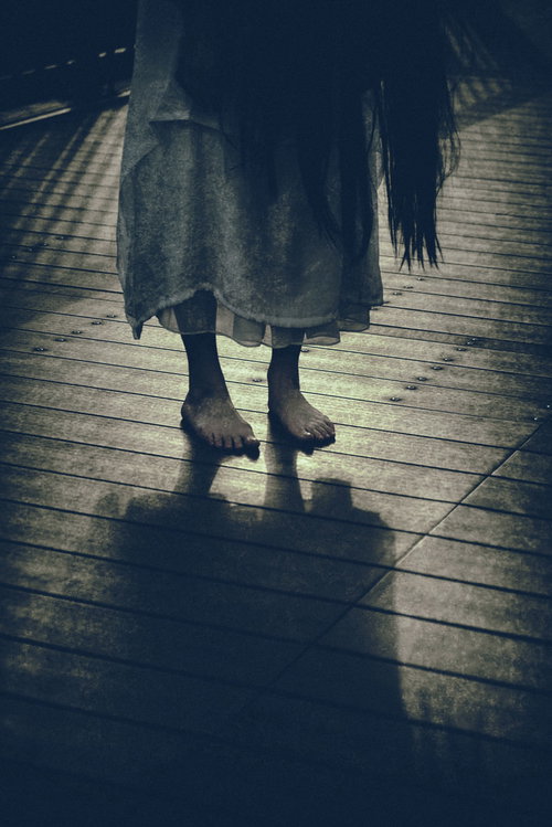 不気味な裸足で立つ女性の足元、薄暗い木製の床に映る呪いの影