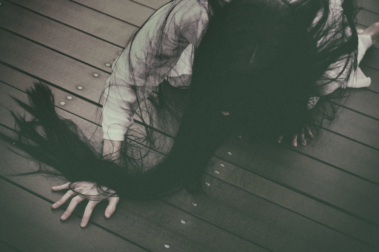 薄暗い木の床を長い黒髪を垂らしながら這って移動する女性［モデル：緋真煉］