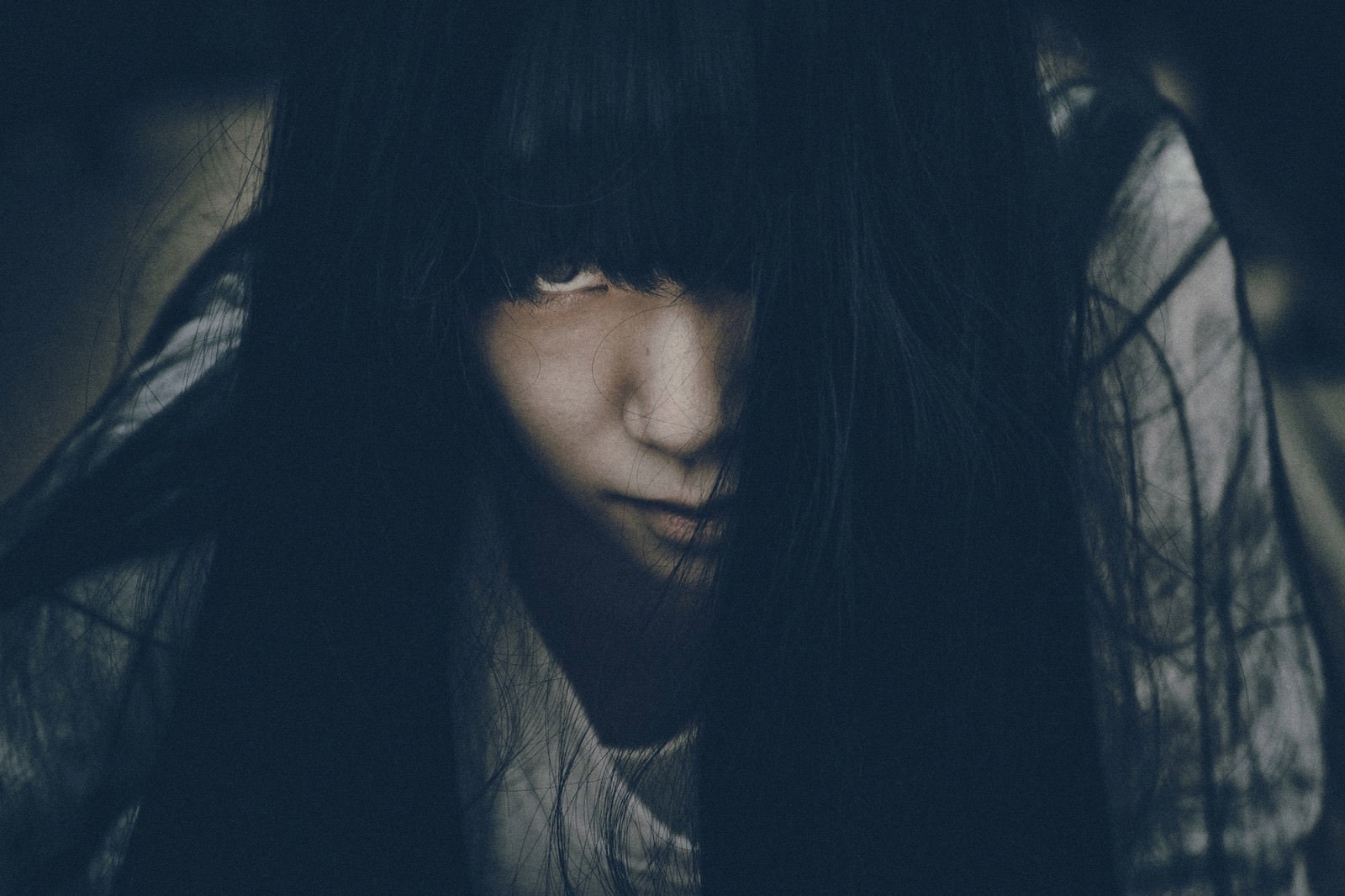 暗闇でフードを被り不気味な眼差しを向ける女性［モデル：緋真煉］