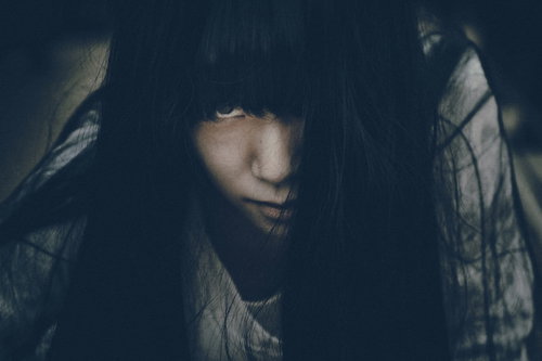 暗闇で怨念のこもった眼差しを向けるフード姿の女性