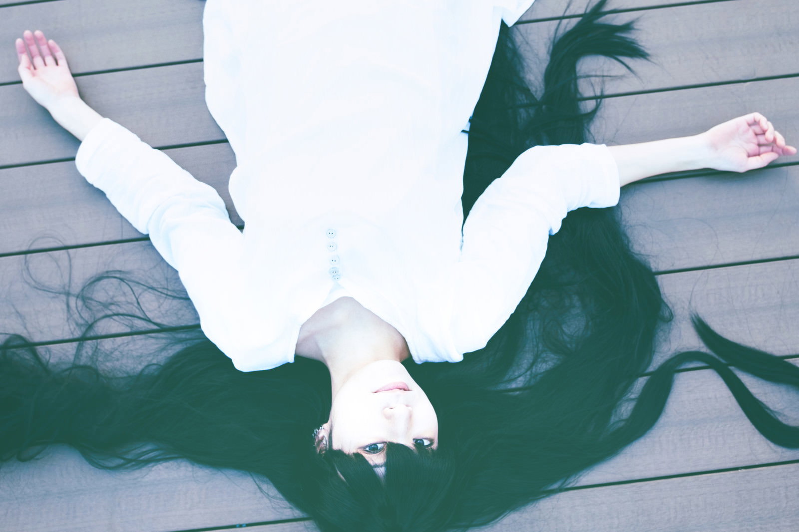 白い服を着た髪の長い女性が木製の床に仰向けに倒れ込んでいる様子［モデル：緋真煉］
