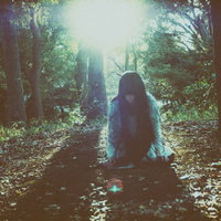 暗い森の中で蹲りながらこちらを睨みつける女性の写真