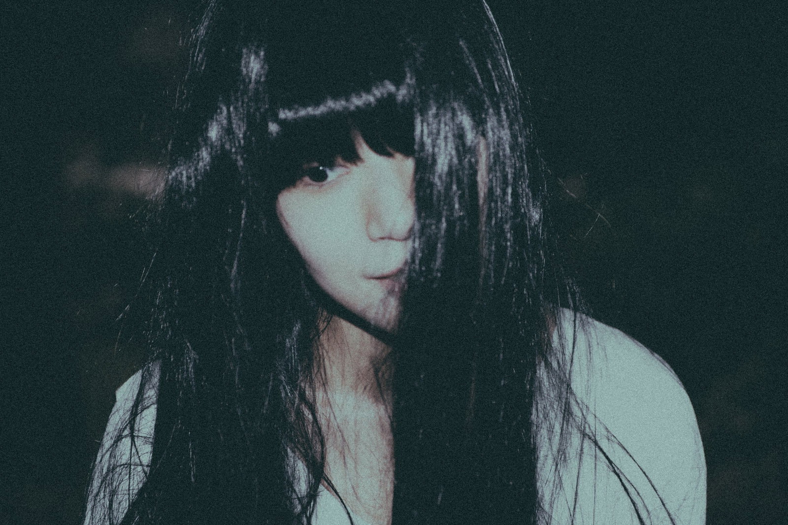 暗闇の中で虚ろな表情を浮かべる長い黒髪の女性［モデル：緋真煉］