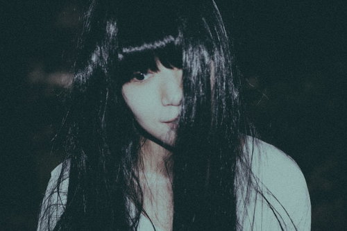 虚ろな表情の長い黒髪の女性の顔アップ、怨念と不安が漂う