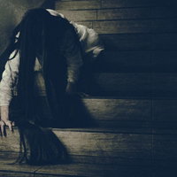 薄暗い木製の階段を這って降りてくる長い黒髪の女性の写真