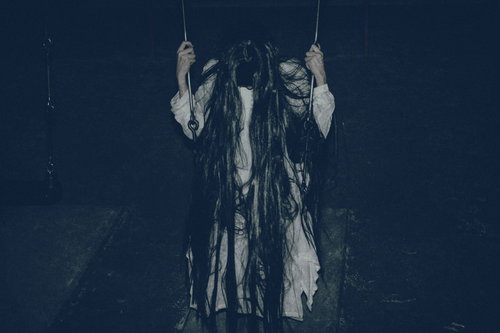 暗い背景で項垂れるブランコに座る髪の長い女性