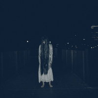 暗闇に立ちすくむ長髪の女性、白い衣服を着た不気味な姿の写真