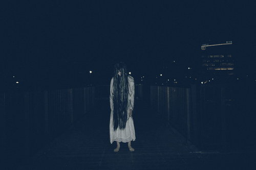 暗闇に立ちすくむ長髪の女性、白い衣服を着た不気味な姿