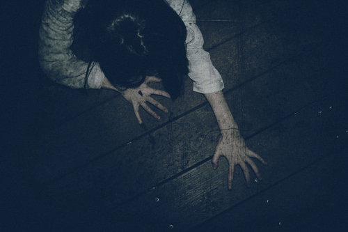 暗闇で爪を立てて這い蹲る長い髪の女性の恐怖シーン