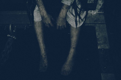 暗い場所で座り込んで手足をぶら下げる女性の姿