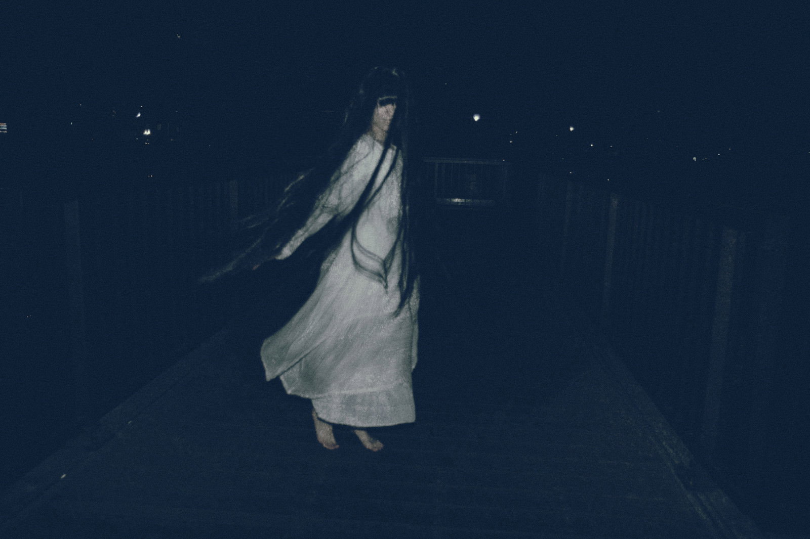 暗闇の夜間でライトに照らされた白い衣装の裸足の女性が立っている［モデル：緋真煉］