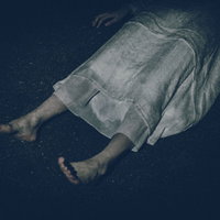 薄暗い背景で横たわる白いワンピースを着た女性の足元の写真