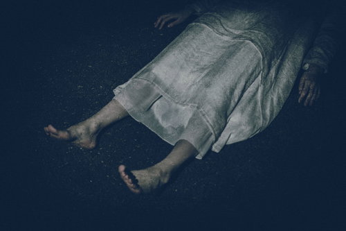 薄暗い背景で横たわる白いワンピースを着た女性の足元