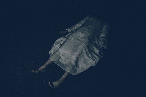 白いワンピースを着て薄暗い空間に横たわる女性の恐怖シーン