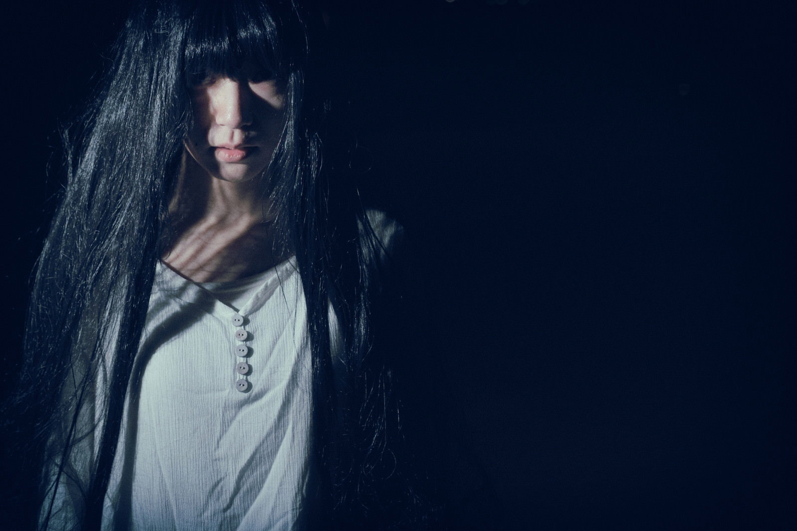 長い黒髪で顔を隠し暗い背景で斜め上を見上げる女性［モデル：緋真煉］