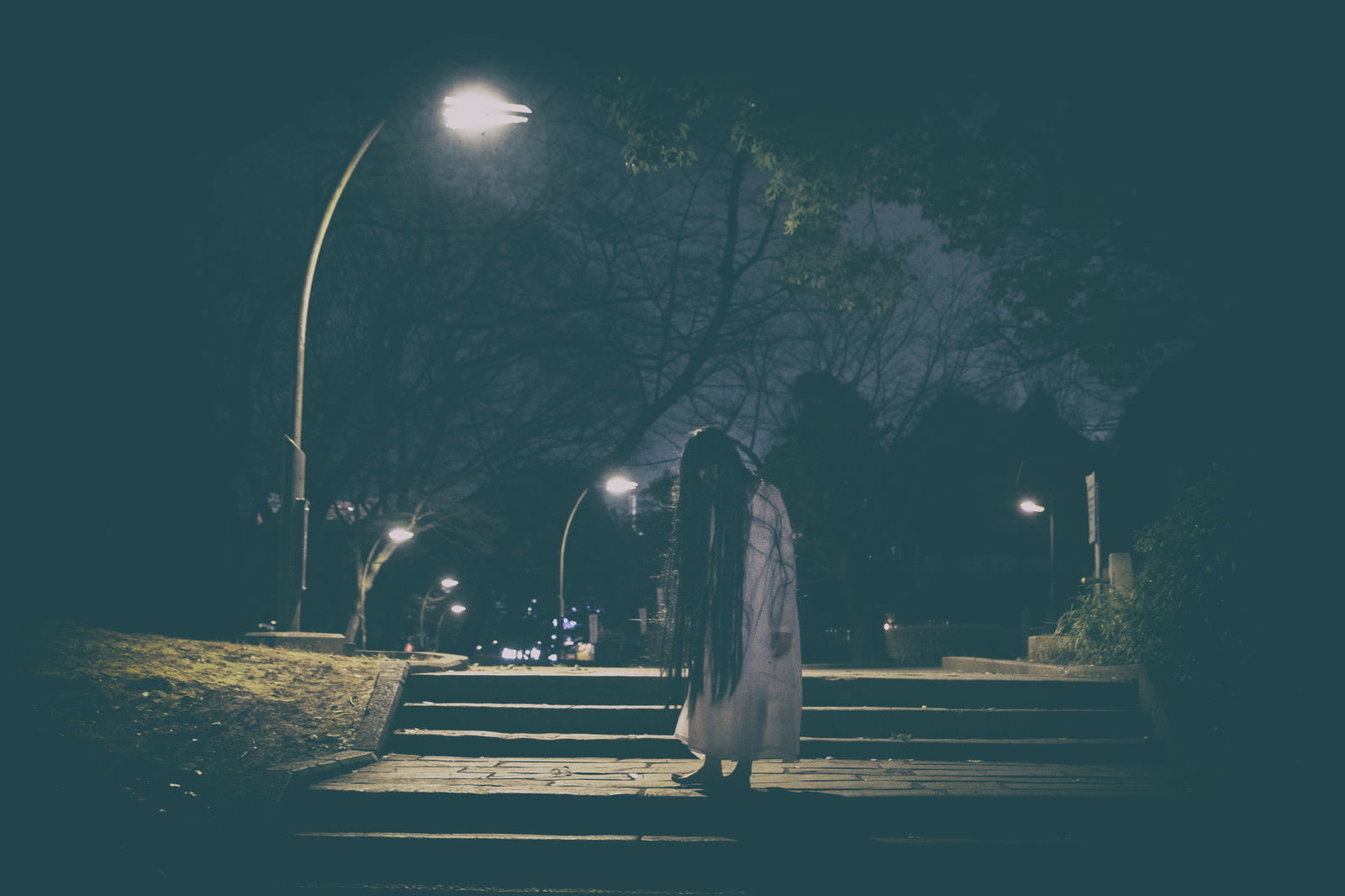 夜の公園の階段を上る髪の長い女性