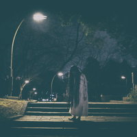 公園のライトの下で佇む髪の長い女性の写真