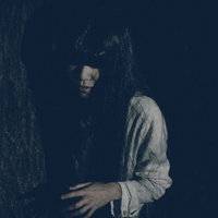 木陰から近づく不気味な白い衣服の女性の暗闇ホラーの写真