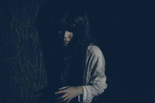 木陰から近づく不気味な白い衣服の女性の暗闇ホラー