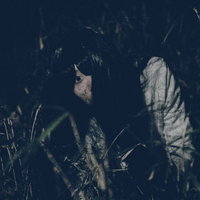 暗闇の草むらを這う髪の長い女性が映るホラーの写真