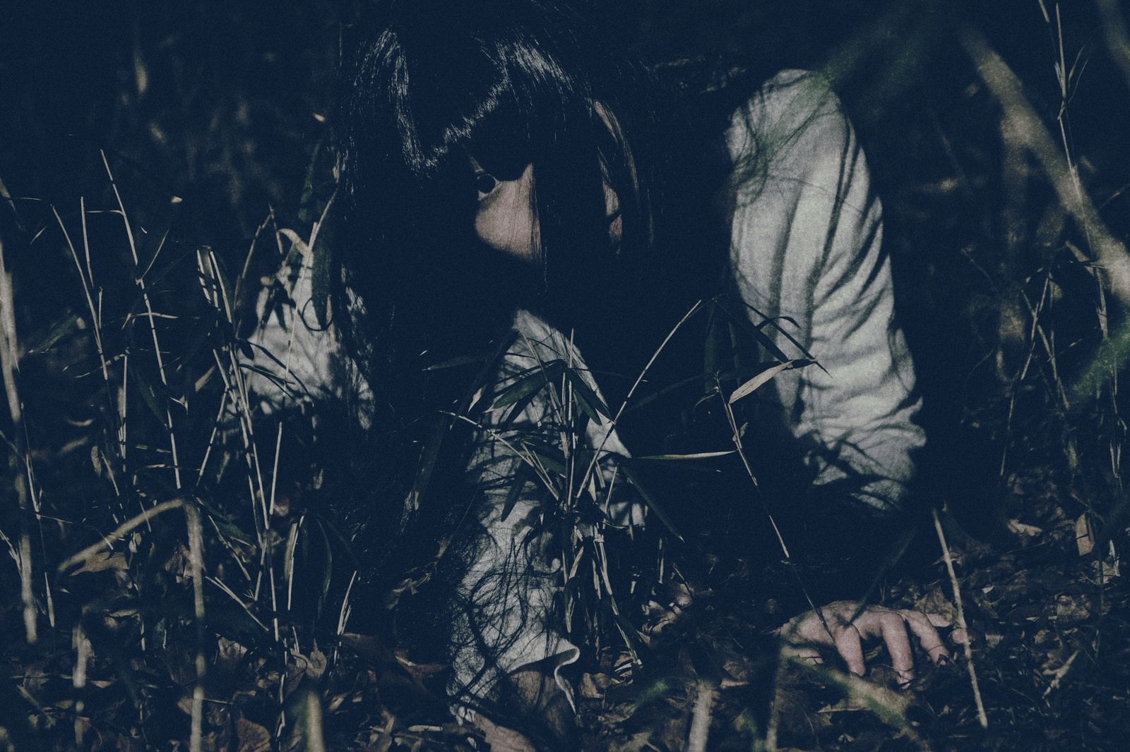 暗闇の草むらで髪の長い女性が這うように移動している不気味な夜のシーン［モデル：緋真煉］