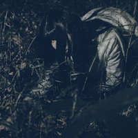 深夜の暗い草むらで落とした小銭を探す女性の写真