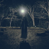 真夜中の雑木林で月明かりに照らされ仁王立ちする女性の写真