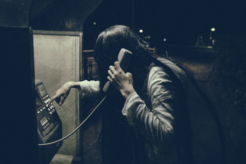 呪いの電話で受話器を握る女性（ストーカー）