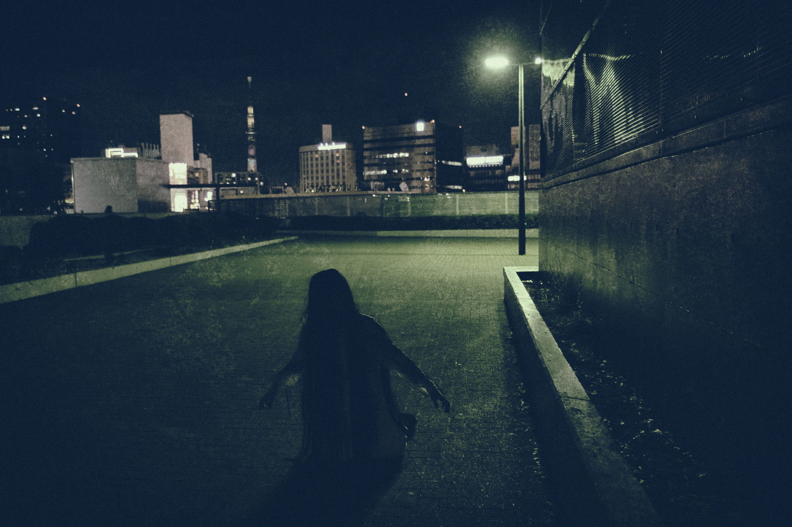 夜の都市部で建物の物陰に膝から崩れ落ちる女性のシルエット［モデル：緋真煉］