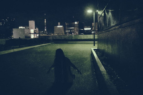 建物の物陰で膝から崩れ落ちる女性の夜景、都市の暗闇でシルエット