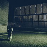 捕まったらゲームオーバー。夜の建物で振り返る白い服の女性の写真