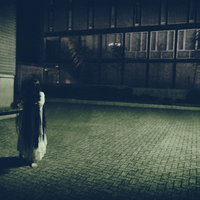 薄暗い石畳の広場へゆっくり近づいてくる白い服の女性の亡霊の写真