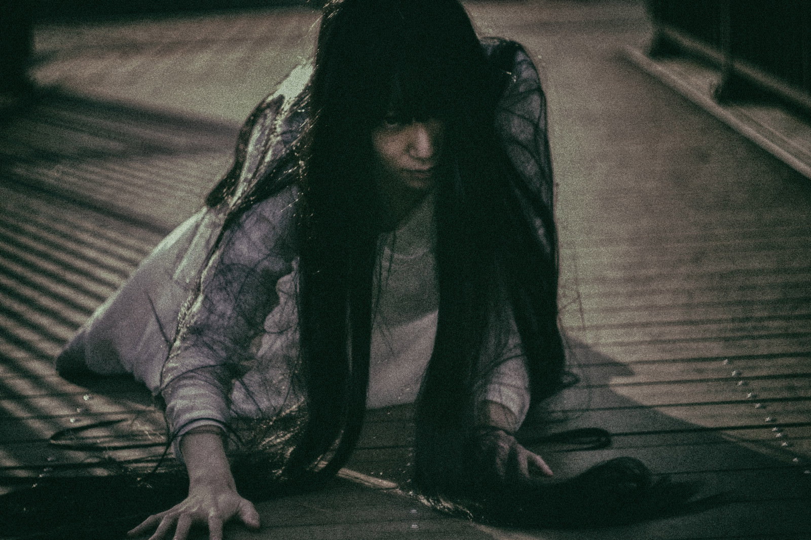 暗闇の中で長い黒髪に顔を覆われながら這いつくばる女性［モデル：緋真煉］