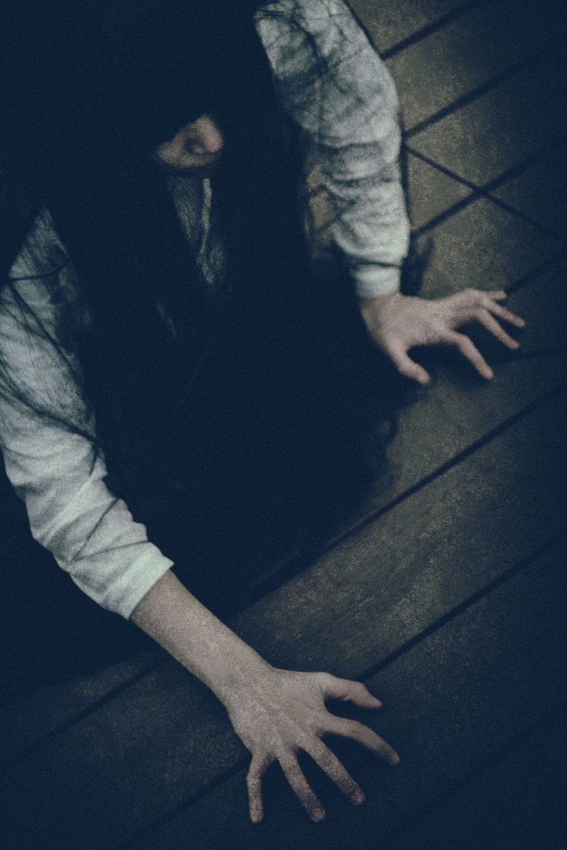 暗闇の中で這うような姿勢をとる白い衣服を着た女性［モデル：緋真煉］