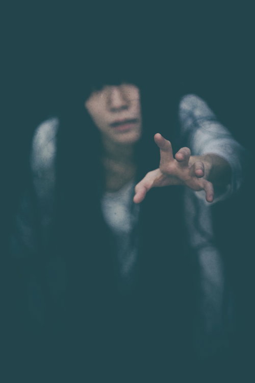 暗闇から手を伸ばして助けを求める女性の恐怖シーン